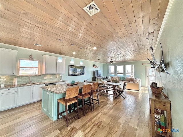 kitchen with light wood finished floors, visible vents, open floor plan, a sink, and backsplash