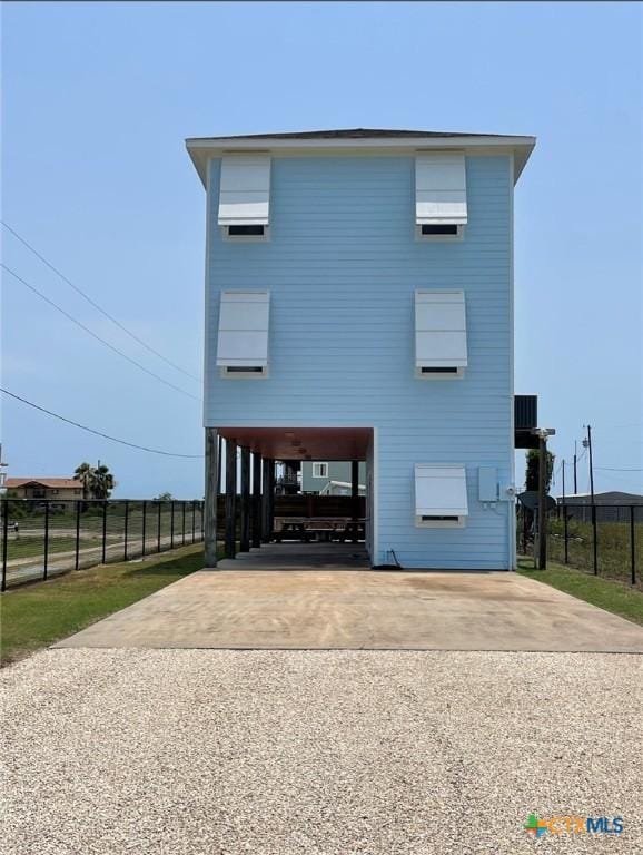 raised beach house featuring a carport, concrete driveway, and fence