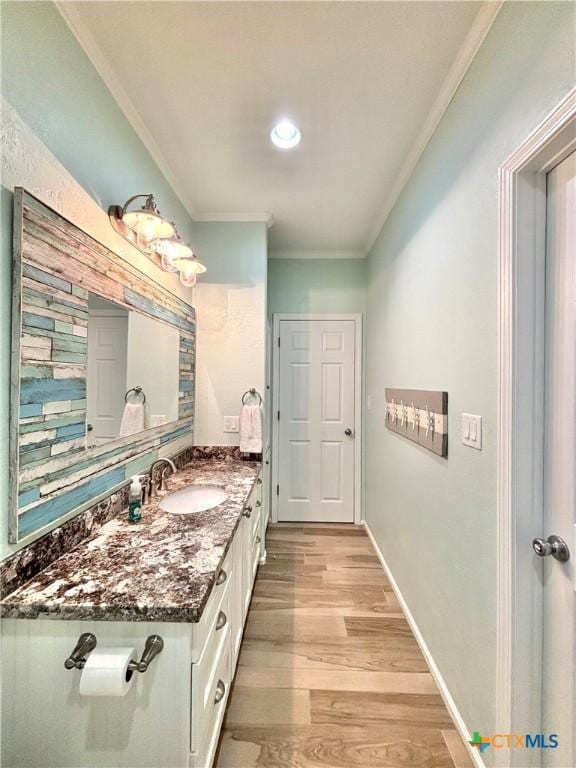 bathroom featuring baseboards, wood finished floors, vanity, and crown molding