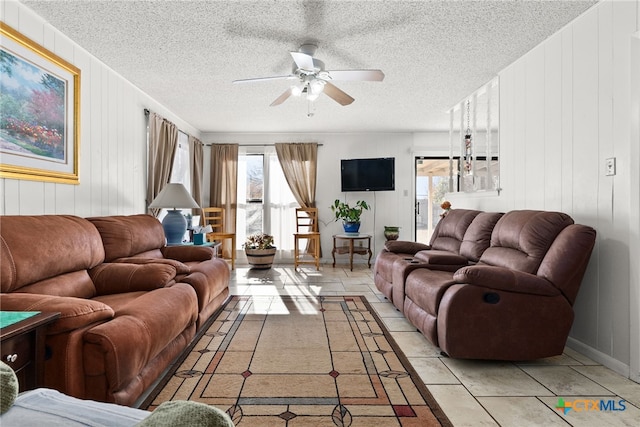 living room with ceiling fan, wooden walls, and a textured ceiling