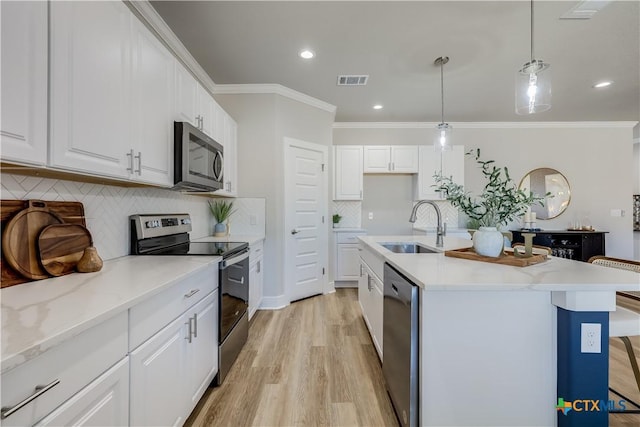 kitchen with hanging light fixtures, appliances with stainless steel finishes, white cabinetry, a sink, and an island with sink