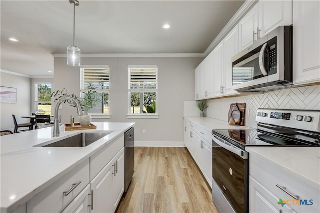 kitchen with hanging light fixtures, appliances with stainless steel finishes, a sink, and white cabinets