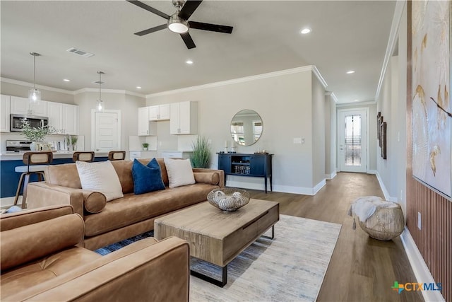 living area with visible vents, baseboards, light wood-style flooring, crown molding, and recessed lighting