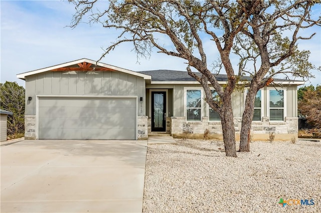 single story home with a garage, stone siding, board and batten siding, and concrete driveway