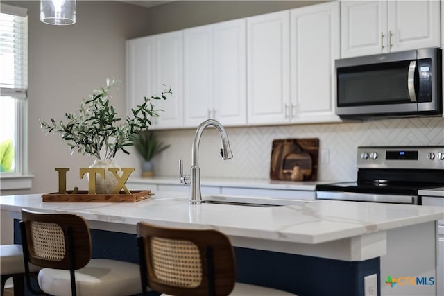 kitchen with white cabinetry, light stone counters, stainless steel appliances, and backsplash