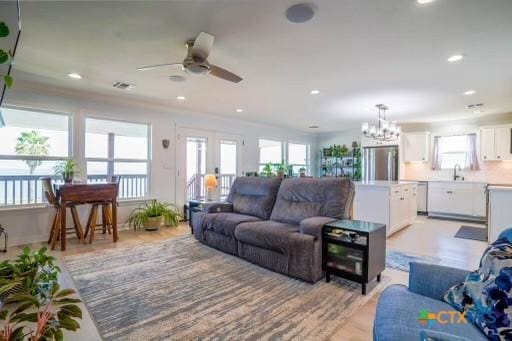 living room with light wood-style flooring, ceiling fan with notable chandelier, recessed lighting, and a wealth of natural light