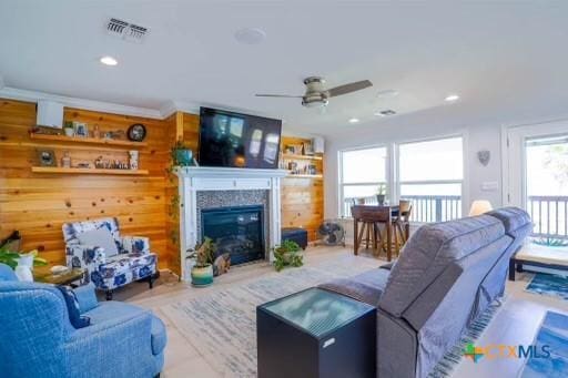 living area featuring wooden walls, a ceiling fan, visible vents, recessed lighting, and a glass covered fireplace