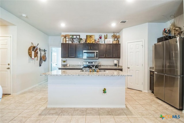 kitchen featuring sink, dark brown cabinets, stainless steel appliances, light stone counters, and a center island with sink