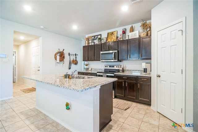 kitchen featuring sink, a kitchen island with sink, light tile patterned floors, stainless steel appliances, and dark brown cabinets