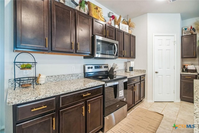 kitchen featuring dark brown cabinetry, light stone countertops, light tile patterned flooring, and appliances with stainless steel finishes