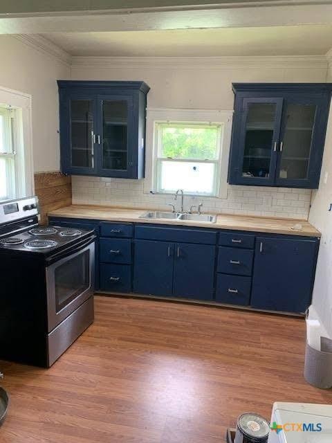 1202 S 7th St, Temple, TX 76504 - kitchen featuring electric stove, blue cabinets, a sink, crown molding, and light wood-style flooring