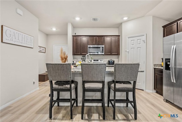 8919 Cantera Ridge Rd, Temple, TX 76502 - kitchen featuring stainless steel appliances, light wood-style floors, dark brown cabinetry, a kitchen bar, and recessed lighting