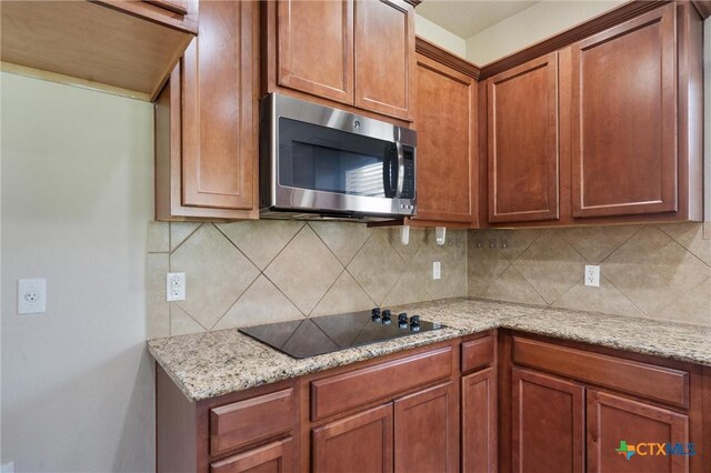 3903 Scenic Trail Dr, Harker Heights, TX 76548 - kitchen featuring stainless steel microwave, black electric stovetop, decorative backsplash, light stone counters, and brown cabinets