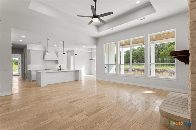 unfurnished living room with light hardwood / wood-style flooring, ceiling fan with notable chandelier, and a raised ceiling