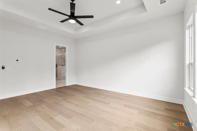 spare room featuring light wood-type flooring, ceiling fan, and a tray ceiling