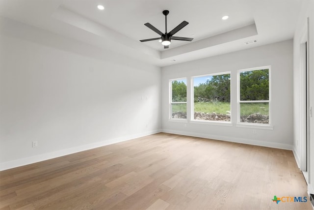 unfurnished room featuring light hardwood / wood-style floors, ceiling fan, and a raised ceiling