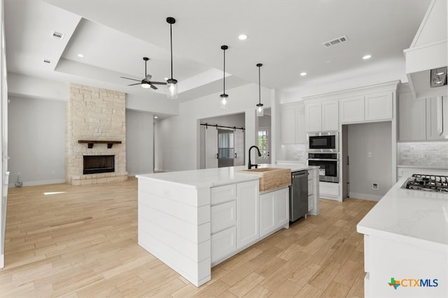 kitchen featuring white cabinetry, a barn door, a center island with sink, and stainless steel appliances