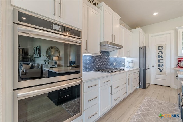 1308 Dancing Oak Ln, San Marcos, TX 78666 - kitchen with under cabinet range hood, stainless steel appliances, light wood-type flooring, white cabinetry, and light countertops