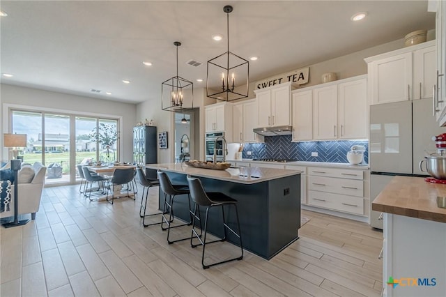1308 Dancing Oak Ln, San Marcos, TX 78666 - kitchen with freestanding refrigerator, under cabinet range hood, backsplash, stovetop, and white cabinets
