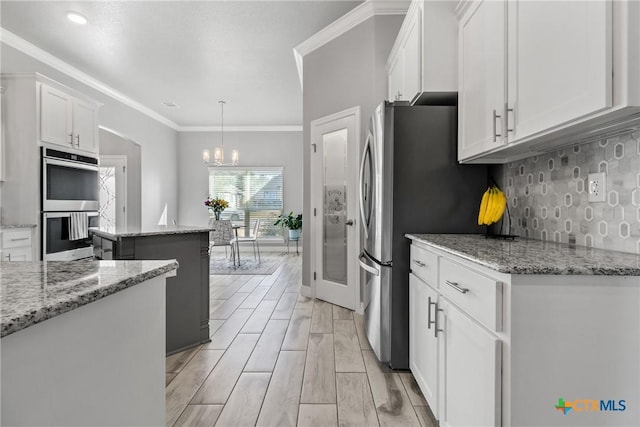 kitchen with white cabinets, a kitchen island, decorative light fixtures, stainless steel appliances, and light stone counters