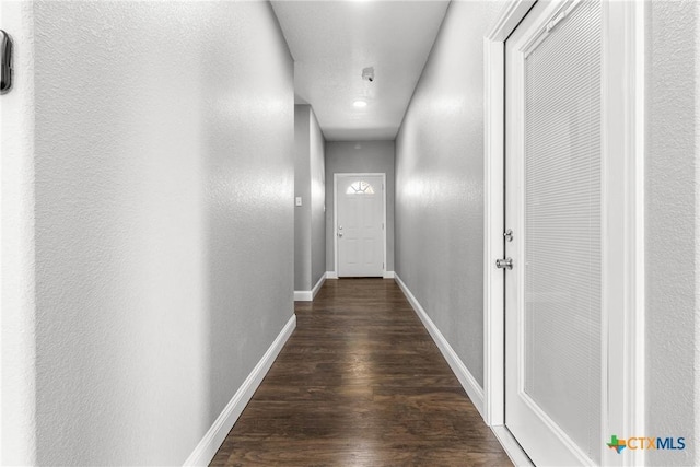 hall featuring a textured wall, dark wood finished floors, and baseboards