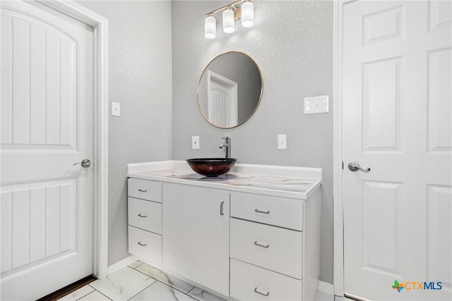 bathroom with marble finish floor, a textured wall, and vanity