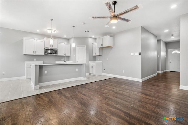 kitchen with light countertops, stainless steel microwave, hanging light fixtures, white cabinetry, and an island with sink