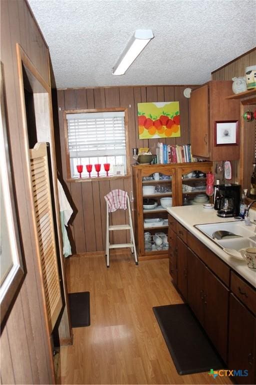 kitchen featuring a textured ceiling, wood walls, sink, and light hardwood / wood-style flooring