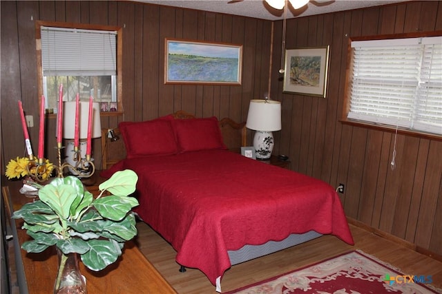 bedroom with ceiling fan, wood-type flooring, and wood walls