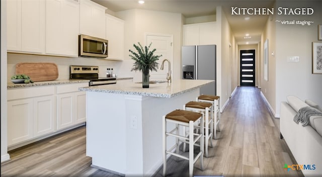 kitchen with stainless steel appliances, light hardwood / wood-style floors, white cabinetry, a center island with sink, and light stone counters