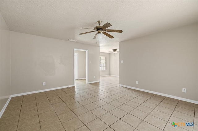 spare room featuring a textured ceiling, light tile patterned floors, baseboards, visible vents, and ceiling fan