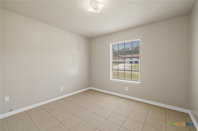 empty room featuring a textured ceiling, baseboards, and light tile patterned floors