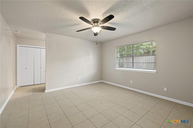 unfurnished room with light tile patterned floors, a ceiling fan, a textured ceiling, visible vents, and baseboards