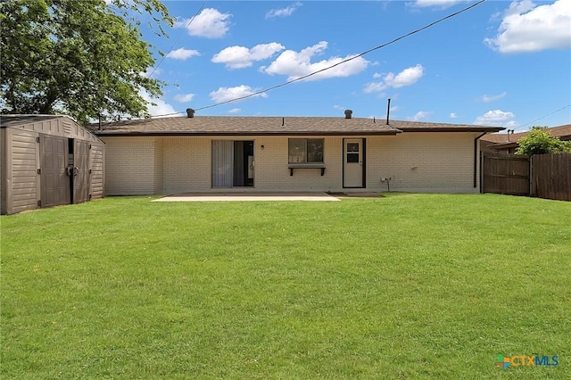 rear view of property featuring fence, brick siding, a yard, a patio, and a shed