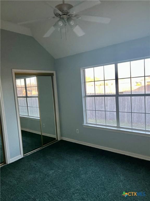 unfurnished bedroom with dark colored carpet, multiple windows, lofted ceiling, and baseboards