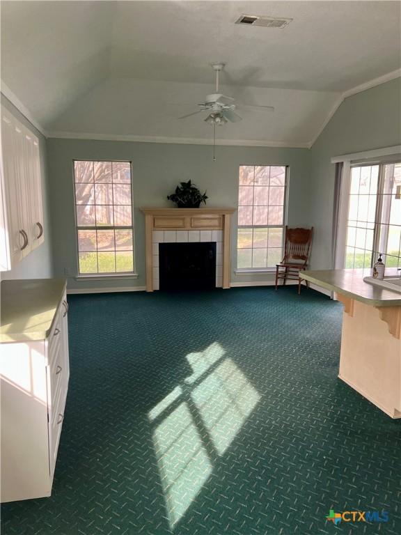 unfurnished living room featuring vaulted ceiling, visible vents, dark colored carpet, and a tiled fireplace