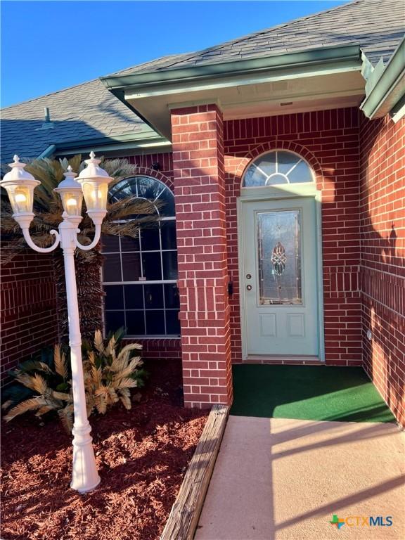 property entrance with brick siding and a shingled roof