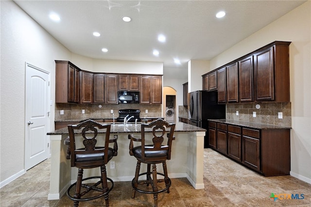 kitchen featuring a center island with sink, dark stone counters, and black appliances