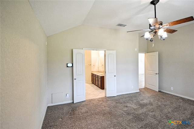 unfurnished bedroom featuring ceiling fan, light colored carpet, ensuite bathroom, and vaulted ceiling