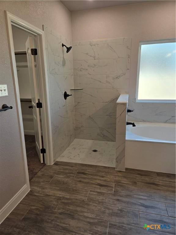 bathroom with a bath, a walk in closet, tiled shower, and wood finished floors