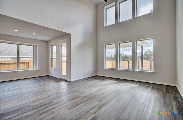 unfurnished living room featuring dark wood-type flooring and a towering ceiling