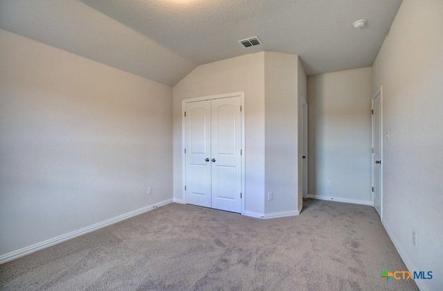 unfurnished bedroom with a textured ceiling, a closet, lofted ceiling, and light colored carpet