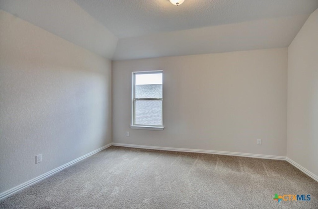 carpeted empty room featuring vaulted ceiling and a textured ceiling