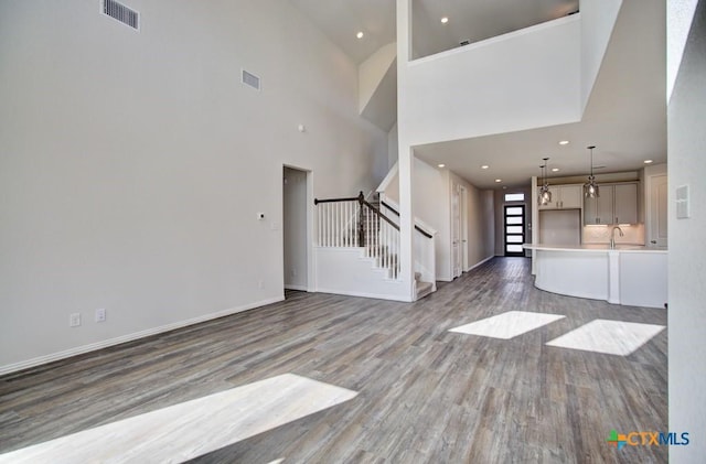 unfurnished living room with a towering ceiling, sink, and hardwood / wood-style flooring