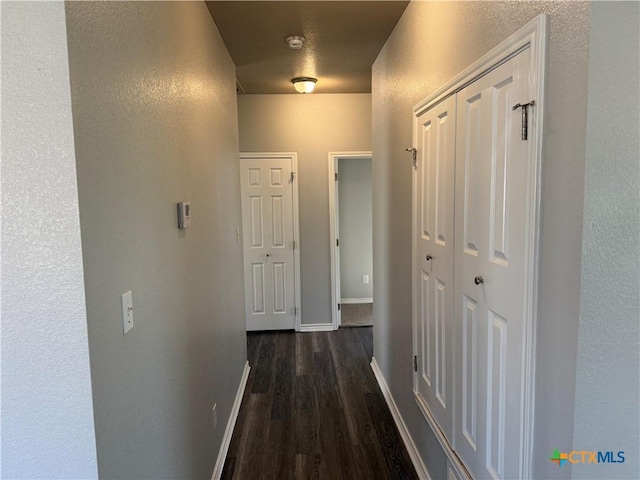 hall with dark wood finished floors, a textured wall, and baseboards