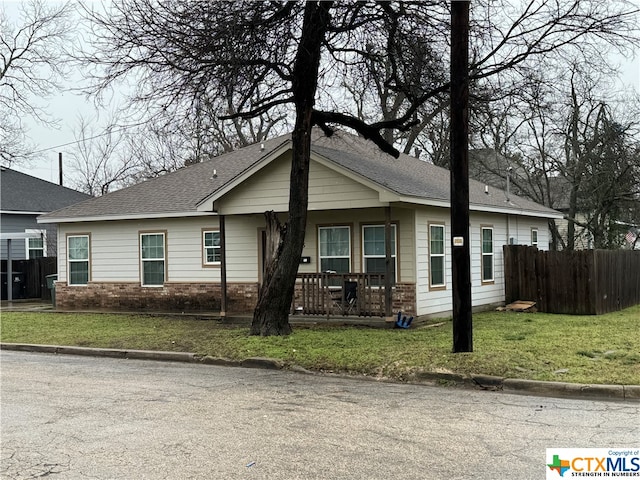 ranch-style home with a front lawn, fence, covered porch, a shingled roof, and brick siding