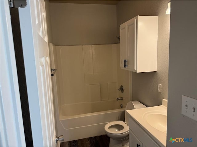 full bath featuring toilet, wood finished floors, tub / shower combination, vanity, and a textured wall