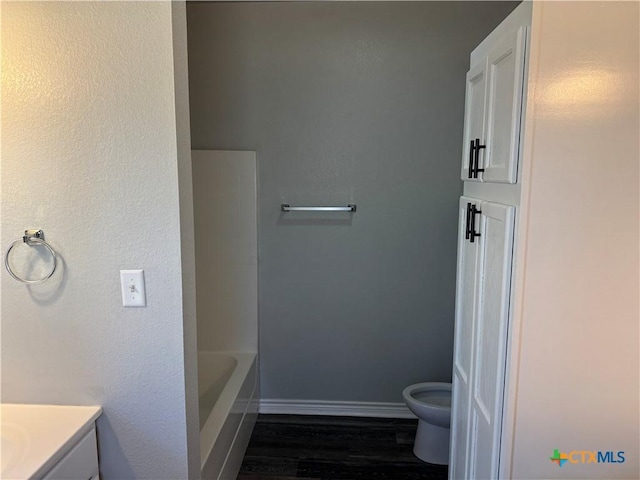 full bathroom featuring baseboards, toilet, a bathtub, wood finished floors, and vanity