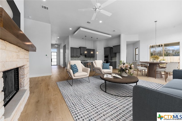 living room with an outdoor stone fireplace, light hardwood / wood-style floors, and ceiling fan