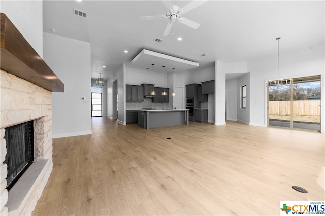 unfurnished living room with light wood-type flooring, a stone fireplace, and ceiling fan